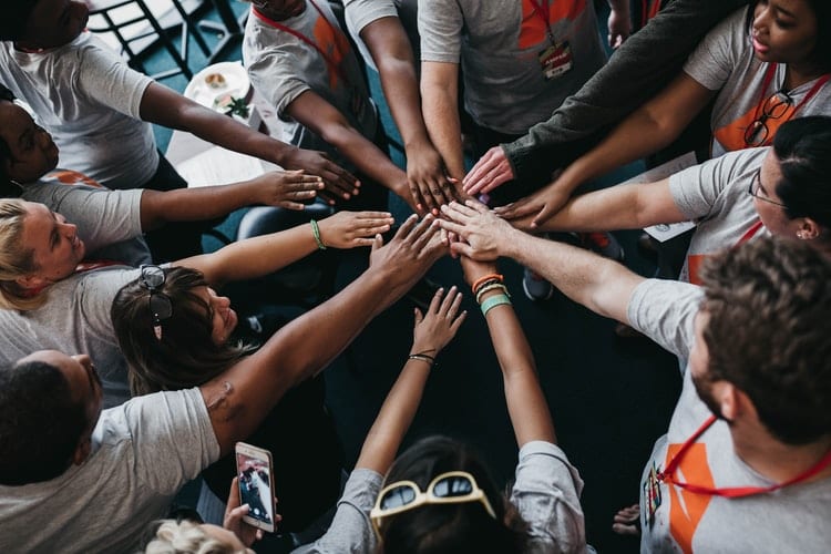 A group standing in a circle with their fingers touching, highlighting a community