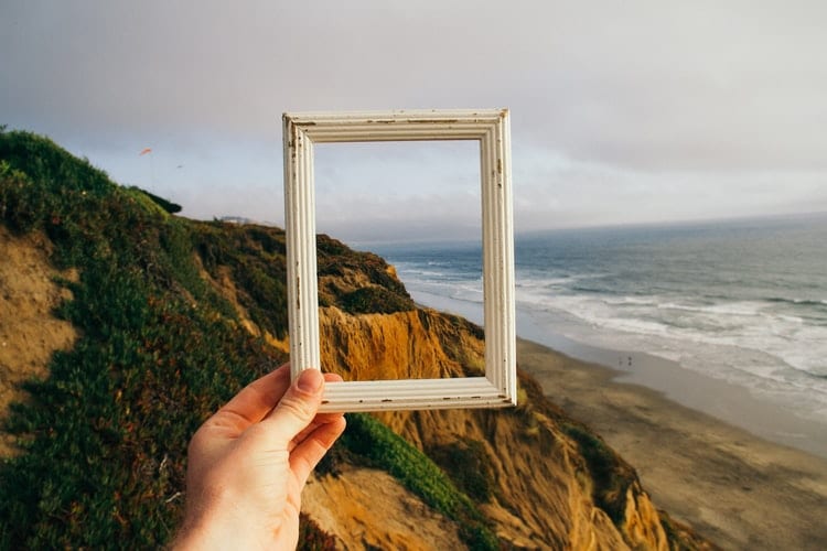 a hand holding an empty picture frame by the coast